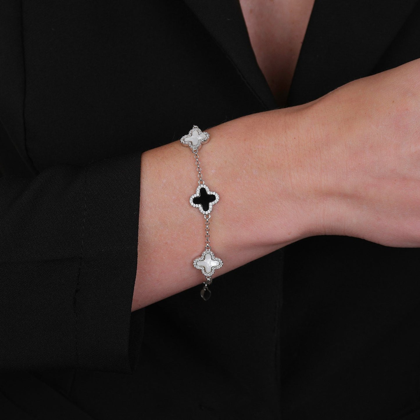 Modelo usando pulseira prateada de trevos pretos e brancos cravejados de zircônia, com banho de ródio branco e acabamento antialérgico