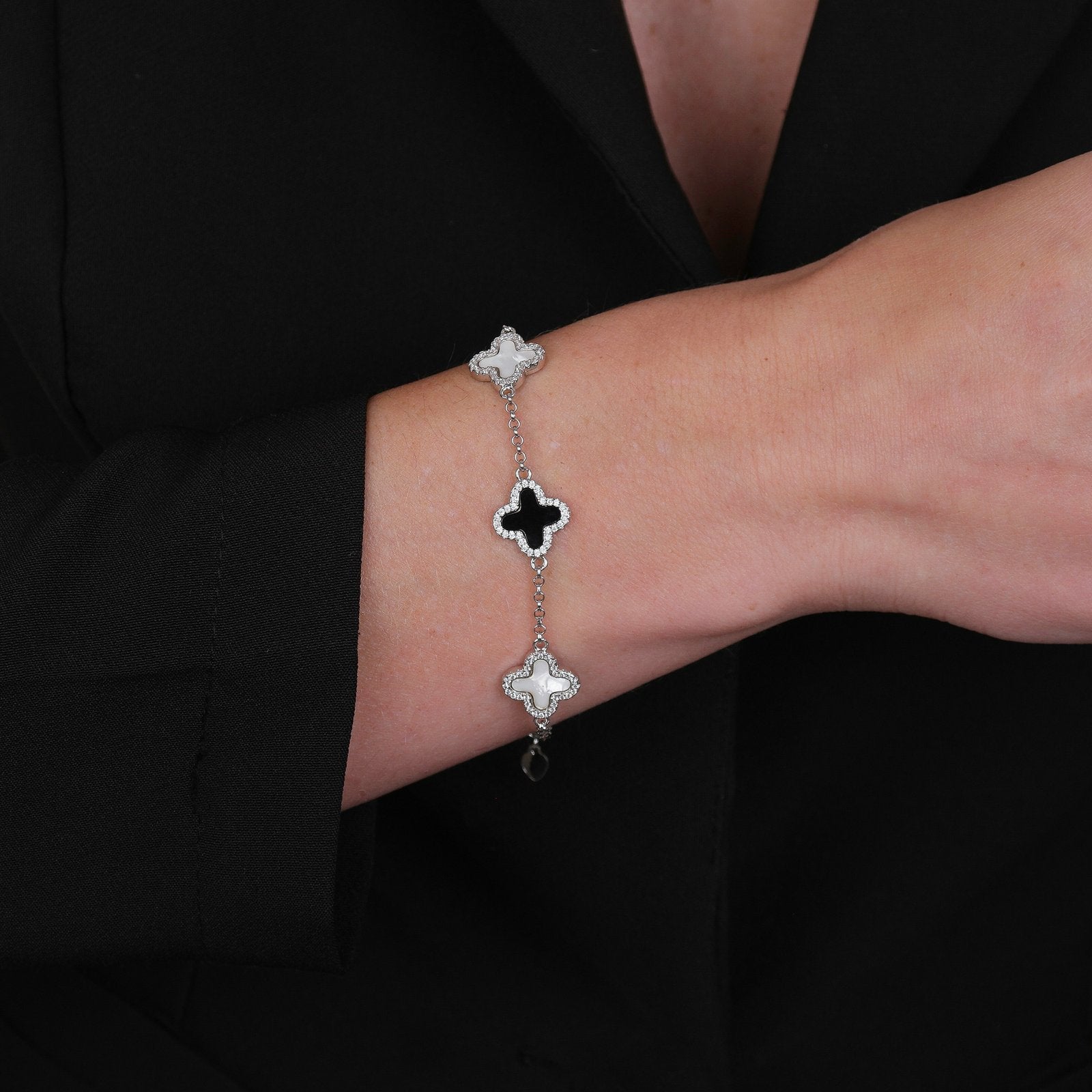 Modelo usando pulseira prateada de trevos pretos e brancos cravejados de zircônia, com banho de ródio branco e acabamento antialérgico